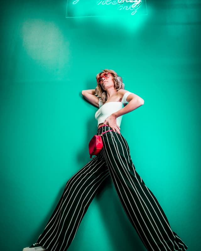 Modelo con top blanco, pantalón palazzo a rayas, cartera roja y lentes rojos